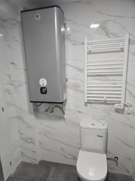 Baño alicatado en mármol blanco con termo eléctrico y radiador toallero