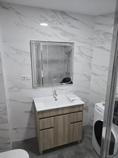 Mueble de baño de madera con lavabo y espejo sobre alicatado marmoleado