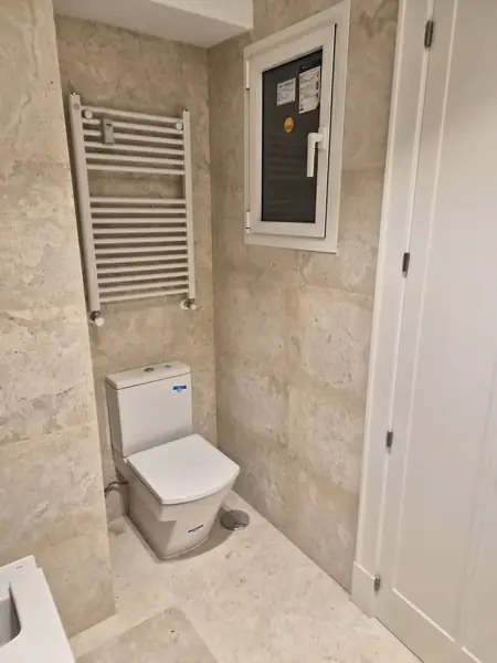 Baño alicatado en travertino con radiador toallero e inodoro